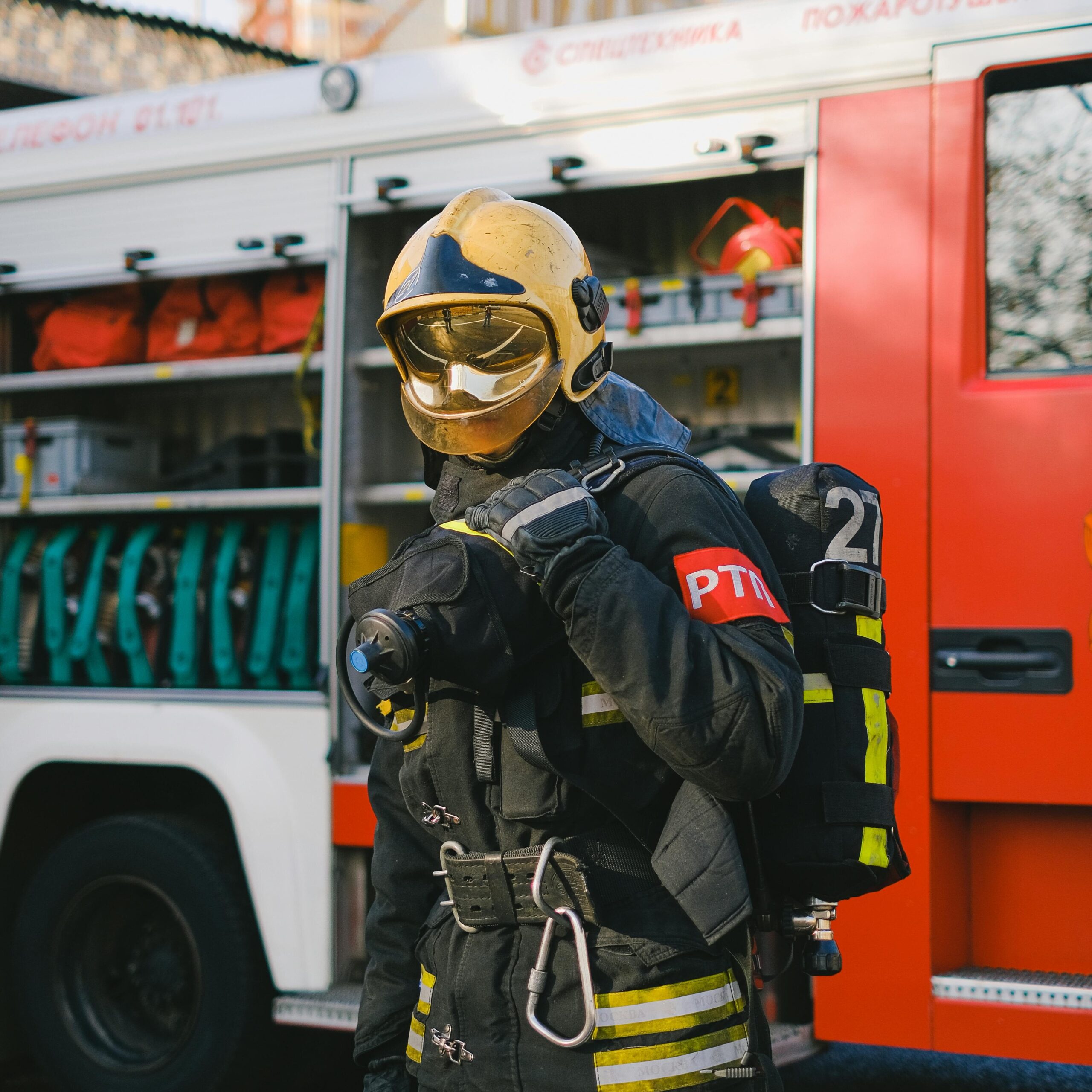 Firefighter in protective gear stands ready beside an equipped fire engine outdoors.